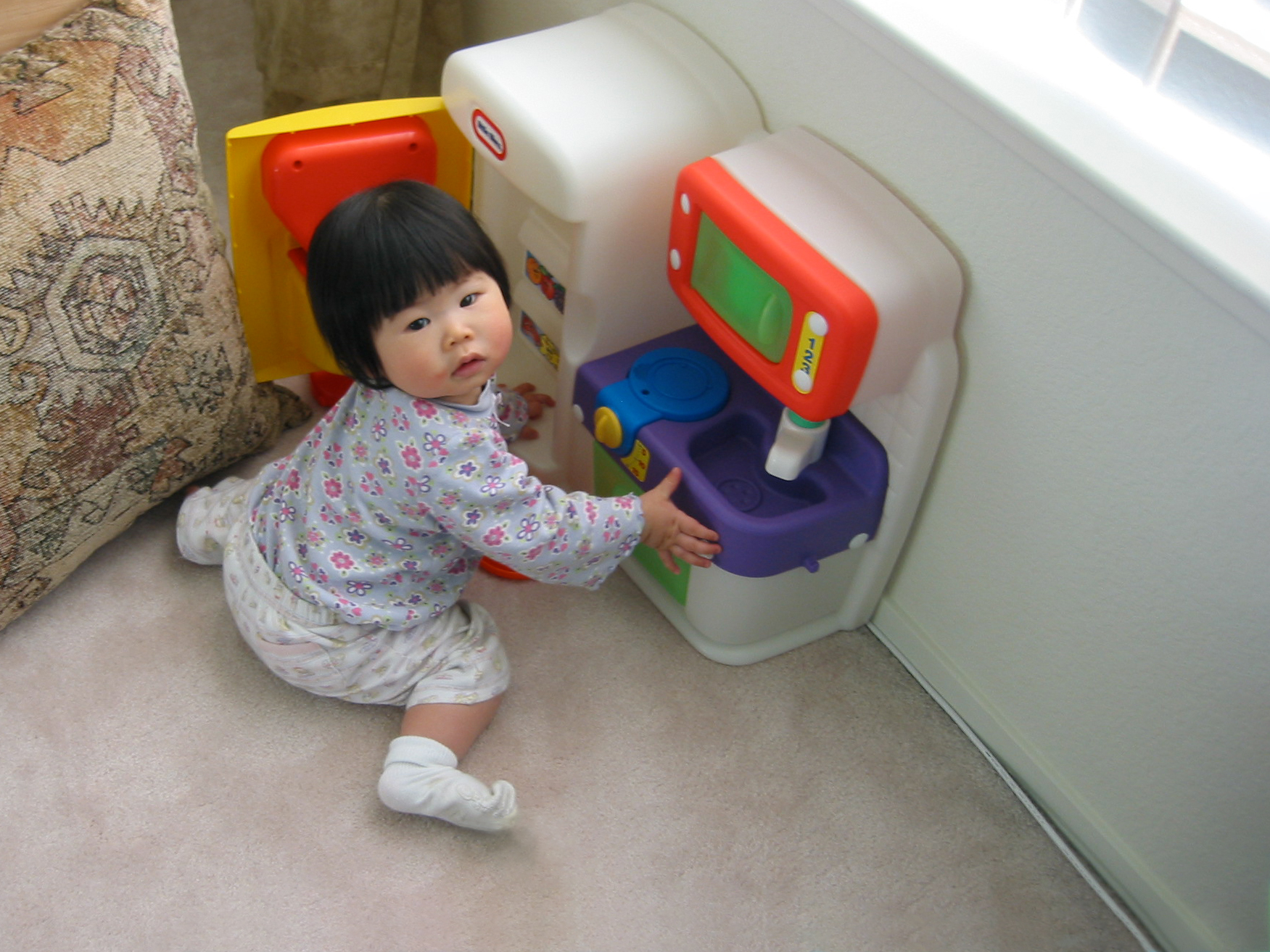 toddler girl sitting on the ground playing with a kitchenette toy